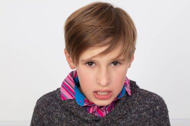 Çizgili gömlekli ve mavi eşarplı bir çocuk suratında somurtkan bir ifadeyle kameraya bakıyor..