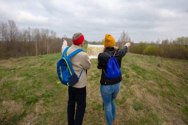 Active elderly Caucasian couple hiking with backpacks poles enjoying their adventure. They are looking at a map or a tourist route.