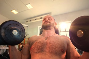 Sakallı adam spor salonunda ağırlık kaldırıyor. Güç ve kararlılık kavramı