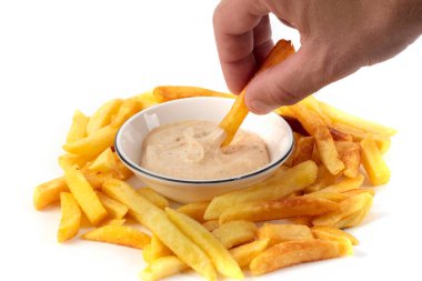 Bir el patates kızartmasını beyaz bir sos kasesine daldırır..