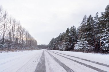Kış otobanı üzerindeki şablonlar dört düz çizgi şeklinde. Karla kaplı ormanın arka planında karlı bir yol. Kış manzarası.