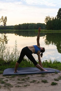 Bir kadın, doğada gölde fizyoterapi egzersizleri yapmakla meşgul. Hastalıkları egzersizle tedavi etme kavramı.