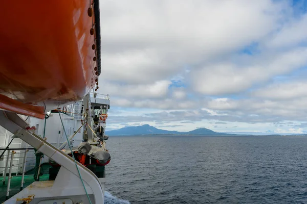 Ufukta yemyeşil adalar belirirken sakin suların üzerinde bir gemi süzülüyor. Yumuşak bulutlar, açık denizde barışçıl bir deniz manzarası yaratıyor..