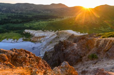 Gün sona ererken tepelerin üzerinden altın güneş ışığı süzülüyor, yemyeşil vadileri ve kayalık uçurumları aydınlatıyor. Bu barışçıl manzara Rusya 'nın uzak bölgesindeki doğanın güzelliğini yansıtıyor..