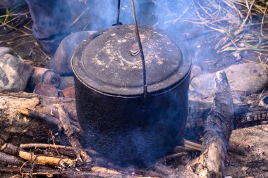Sağlam bir tencere, Rusya 'da engebeli bir manzarayla çevrili, çatırdayan bir ateşin üzerinde oturur. Duman havaya yükselir, vahşi doğada rahat bir atmosfer yaratır..
