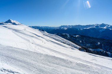 Dağın yamacı. Ön planda güzel karlı dağlar ve vadi manzarası var. Parlak kış güneşi kar beyazı manzaraları vurgular.