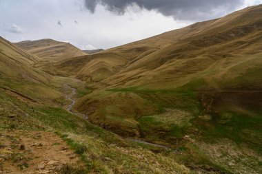 Bulutlu bir gökyüzünün altında nehir akan manzaralı dağ vadisi. Dağıstan Rusya.