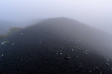 Rusya 'daki yoğun sisten gizemli bir volkanik tepe çıkıyor ve ürkütücü ama güzel bir atmosfer yaratıyor. Koyu toprak ve seyrek bitki örtüsü bölgenin jeolojik tarihine dair ipuçları veriyor..