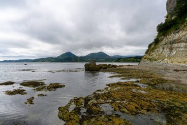 Rusya 'nın sakin bir kıyı şeridinde bulutlu gökyüzü süzülüyor. Uzak dağlar nefes kesici bir zemin oluştururken, kayalık oluşumlar sudan ortaya çıkar, keşif ve yansımaya davetiye çıkarır..