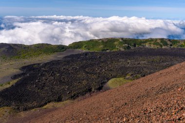 Yüksek bir bakış açısından, volkanın engebeli arazisi yemyeşil ve beyaz bulutlarla çelişiyor. Doğanın güzelliği her yönden gözler önüne seriliyor, keşif ve hayranlık uyandırıyor..