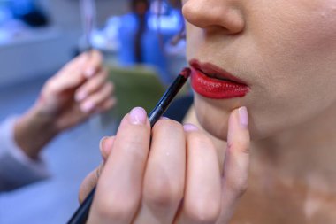 Parlak ve misafirperver bir güzellik salonunda, bir makyöz müşterisinin dudaklarına canlı kırmızı ruj sürüp ustalık ve detaylara dikkat çeker..
