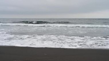 Yumuşak dalgalar yavaşça Kunashir Adası 'nın karanlık kumlarına yuvarlanıyor. Huzurlu deniz, kumsalın sakin bir anında doğanın güzelliğini ortaya çıkaran grinin gölgeleriyle boyanır..