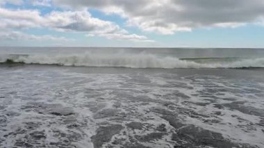 Kunashir Adası 'nın sakin güzelliğini hissedin. Dalgalar yavaşça kumlu kıyıya çarpıyor. Huzurlu manzara bulutlu gökyüzünün altında denizin büyüleyici ritmini sergiliyor..