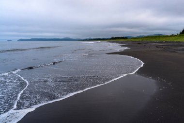 Rusya 'da bulutlar gökyüzünü örterken yumuşak dalgalar karanlık kumlu kıyılara çarpıyor. Huzurlu manzara, kıyı şeridinin doğal güzelliği arasında sessiz bir yansımayı davet eder..