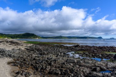 Rusya 'da kayalık kıyıların sakin denizle buluştuğu sakin bir plajda bulutlar tembelce sürükleniyor. Bereketli yeşillik ve uzak tepeler barışçıl bir doğal manzara yaratır..
