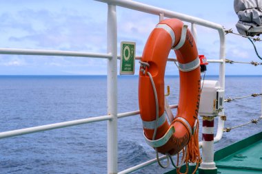 Canlı bir yaşam şamandırası, yumuşak bir gökyüzünün altındaki sakin mavi denizi gören bir geminin korkuluğunda asılı duruyor. Bu ayar, Rusya 'daki deniz maceraları sırasında alınan güvenlik tedbirlerini vurguluyor.