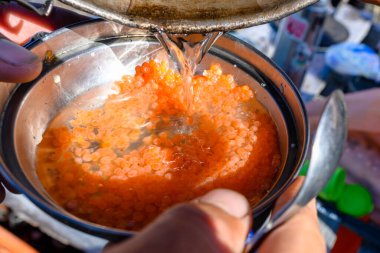 Eller, hareketli bir Rus pazarında parlak turuncu somon yumurtasını süzüyor ve yerel mutfağın canlı özünü yakalıyor. Sahne yemek hazırlama sanatını ve geleneğini yansıtıyor..