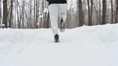 Bir adam karlı bir ormanda hızlı adımlar atar, ayak izleri taze tozda bir yol açar. Kalın kar ağaçları örtüyor, girdap gibi kar taneleriyle dolu büyülü bir kış atmosferi yaratıyor..