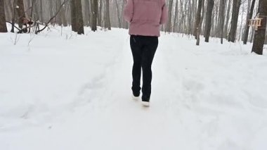 Karlı bir ormanda, genç bir sporcu zarif bir şekilde koşar, bacakları taze karda ritmik olarak hareket eder. Sahne, kış manzarasının ortasında bir rahatlama ve sükunet anı yakalıyor..