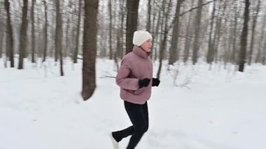 Genç bir kadın, kış soğuğunu kucaklayarak, neşeli bir şekilde karlı bir ormanda koşuyor. Derin kar, o egzersiz yaparken izleri örtüyor, dingin sahnede sağlık ve mutluluk yayıyor..