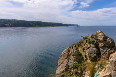 Rusya 'da sakin bir sahil şeridi boyunca huzurlu bir manzara gözler önüne seriliyor. Yumuşak dalgalar kayalık kıyıya vururken yeşil tepeler parlak mavi gökyüzünün altında yükseliyor..