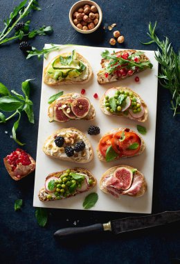 Mermer servis tabağındaki malzemelerle çeşitli bruschetalar. Şarap için atıştırmalık parmak yemeği. Üst görünüm 