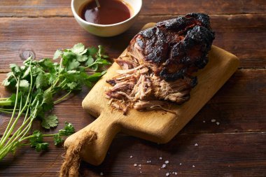 Barbekü soslu domuz eti ve ahşap kesim tahtasında otlar.