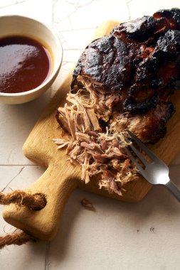 Barbekü soslu domuz eti ve ahşap kesim tahtasında otlar.