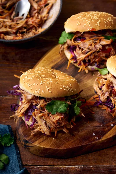 Pulled pork burgers with pickled and fresh vegetables and coriander on brown wooden background