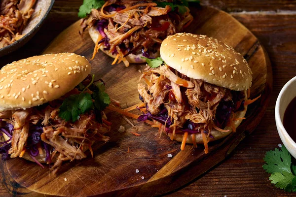 Pulled pork burgers with pickled and fresh vegetables and coriander on brown wooden background