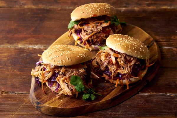 Pulled pork burgers with pickled and fresh vegetables and coriander on brown wooden background