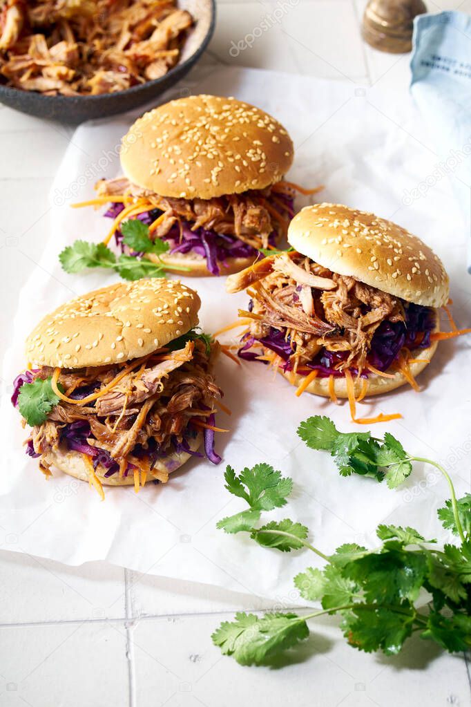 Pulled pork burgers with pickled and fresh vegetables and coriander on white tiled background