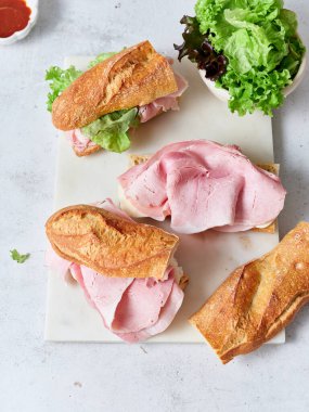 Taze sandviçler baget, jambon, mozzarella ve salatayla birlikte hazır. Bu yemek rahat bir kahvaltı için hazırlandı..