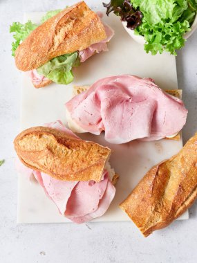 Yemek masasında jambon, mozzarella peyniri ve marullu dilimlenmiş baget sandviçler var..