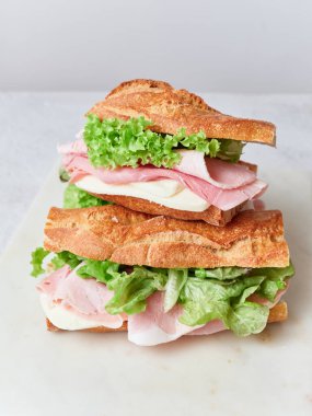 Öğle yemeği veya kahvaltı masasında jambon, mozzarella ve marullu dilimlenmiş sandviçler var. Taze portakallar ve çırpılmış yumurtalar da basit bir yemek için masada..