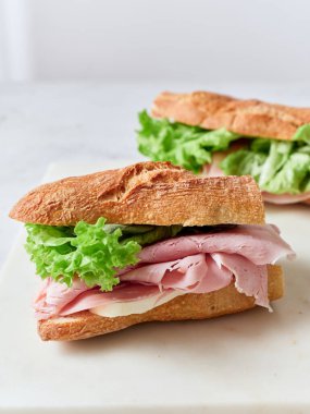 Yemek masasında baget, mozzarella, marul ve jambonlu dilimlenmiş sandviçler var..