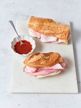 Yemek masasında mozzarella peyniri, jambon ve domates sosuyla yapılan dilimlenmiş baget sandviçler var..