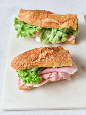 Yemek masasında baget, mozarella peyniri, marul ve jambonlu sağlıklı sandviçler var..