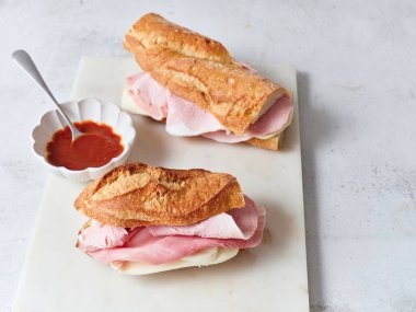 Bir masa mozzarella peyniri ve jambonla dolu iki dilimlenmiş baget sandviçle hazırlandı. Yakınlarda bir kase domates sosu duruyor..