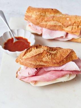 Yemek masasında baget, mozzarella peyniri, jambon ve maruldan yapılmış sağlıklı bir sandviç var..