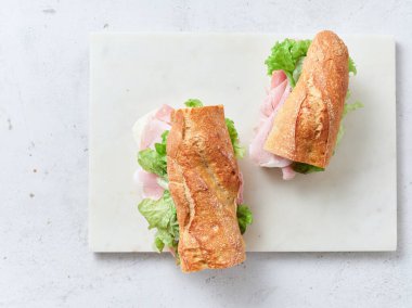 Masada jambon, mozzarella, marul ve baget dilimlenmiş sandviçler var. Taze portakallar ve çırpılmış yumurtalar da mevcuttur ve sağlıklı bir kahvaltı ortamı yaratır..