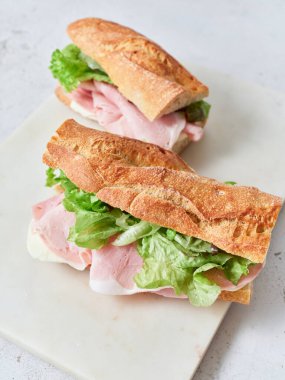 Ekmek, mozarella peyniri, marul ve jambondan yapılmış iki sağlıklı sandviç bir masada oturur..