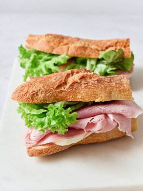 Yemek masasında baget, mozzarella peyniri, jambon ve maruldan yapılmış dilimlenmiş sandviç var..