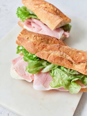 Ekmek, mozarella peyniri, jambon ve yeşil yaprak marulundan yapılmış sandviçler masada oturur..