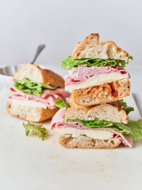 Yemek masasında baget, mozzarella peyniri, jambon ve marul dolu taze sandviçler var..