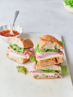 Baget, mozarella peyniri, jambon ve maruldan yapılmış dilimlenmiş sandviçler masaya oturur. Domates sosu yakınlarda..