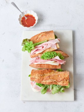 Öğle yemeğinde baget, mozzarella peyniri, jambon, marul ve domates sosuyla yapılan dilimlenmiş sandviçler yer alıyor..