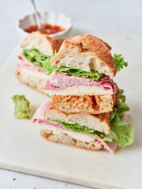 Yemek masasında baget, mozzarella peyniri, jambon, marul ve domates sosundan yapılmış sağlıklı sandviçler var..