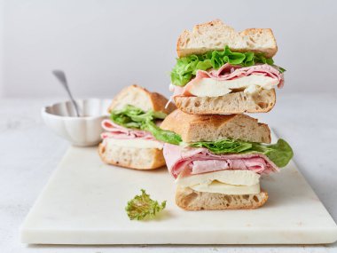 Yemek masası dilimlenmiş baget sandviçlerle dolu. Jambon, mozzarella peyniri ve marul..