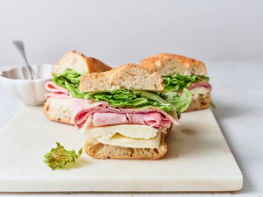 Kahvaltı ya da yemek masasında jambon, mozzarella peyniri ve marul katmanlı sağlıklı bir sandviç bulunur..